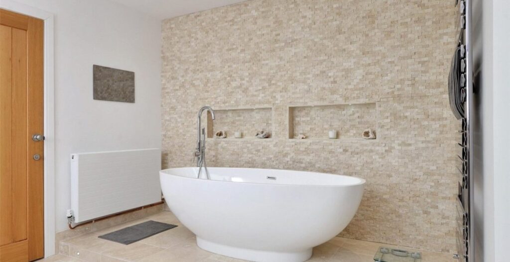 The Lake House, Market Bosworth: bathroom with freestanding bath against a stone feature wall